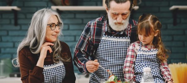 Grandparents and granddaughter preparing salad in home kitchen, creating memories together.
