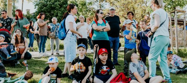 A diverse group of families and children enjoying an outdoor event on a sunny day in a park setting.
